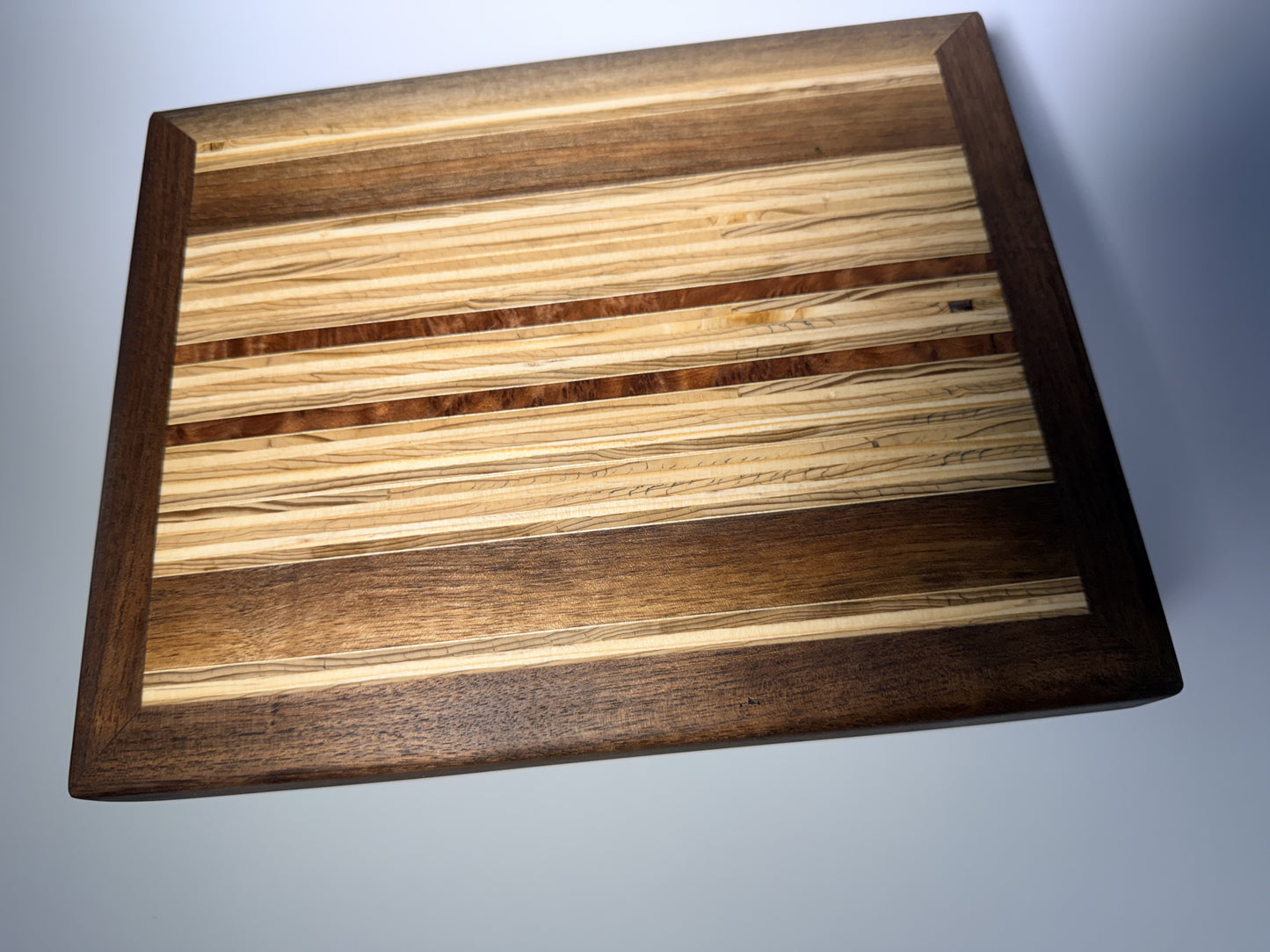 Walnut-framed cutting board with striped inlay center — front three-quarter view