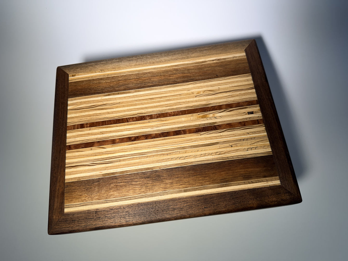 Walnut-framed cutting board with striped inlay center — full face view