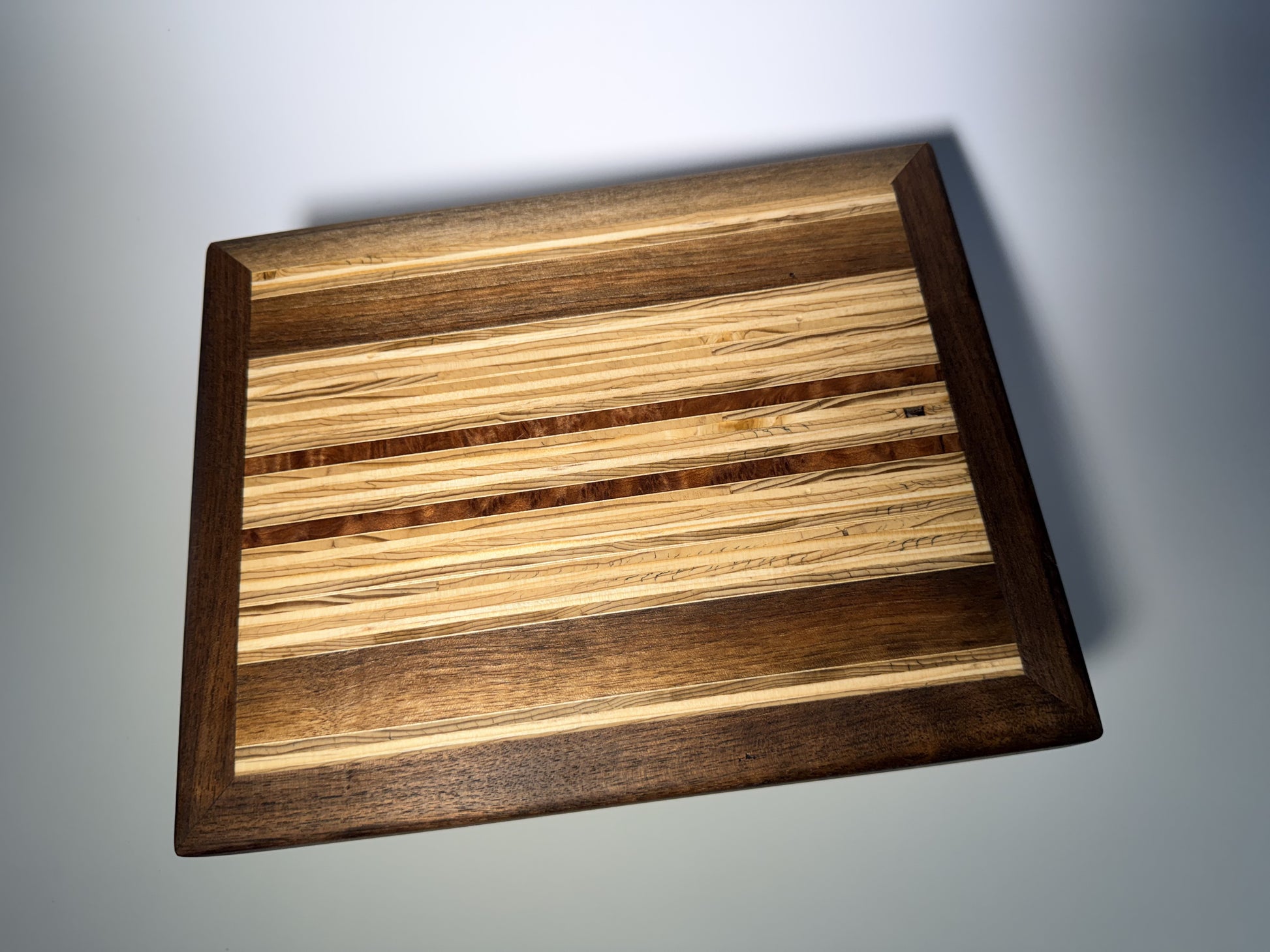 Walnut-framed cutting board with striped inlay center — full face view