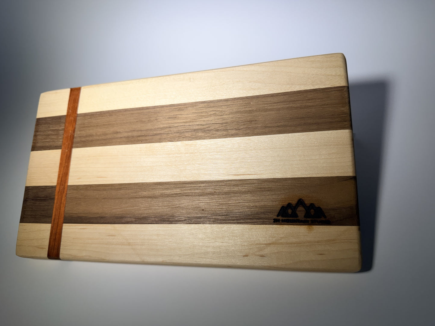 Walnut and maple striped cutting board with straight padauk line — front three-quarter view