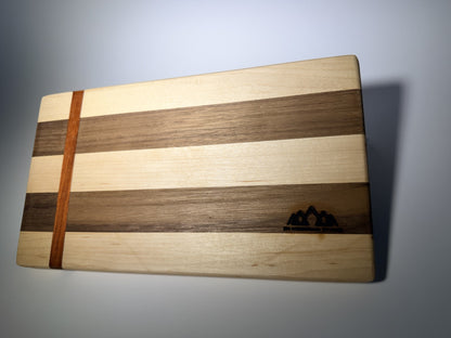 Walnut and maple striped cutting board with straight padauk line — front three-quarter view