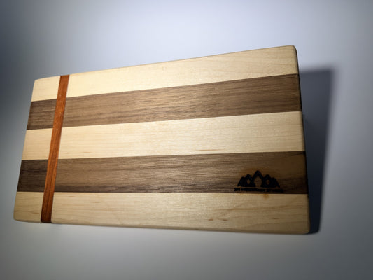 Walnut and maple striped cutting board with straight padauk line — front three-quarter view