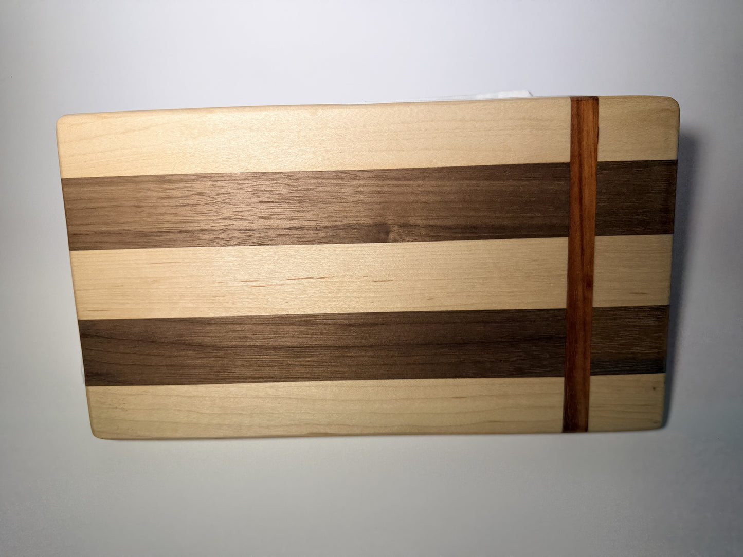 Walnut and maple striped cutting board — top view with padauk accent