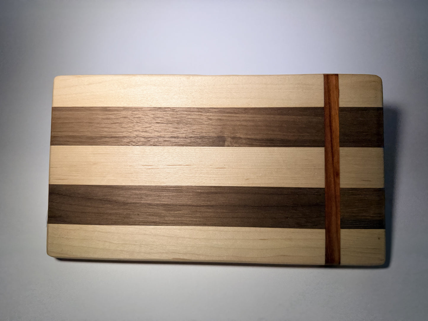 Walnut and maple striped cutting board with straight padauk line — full face view