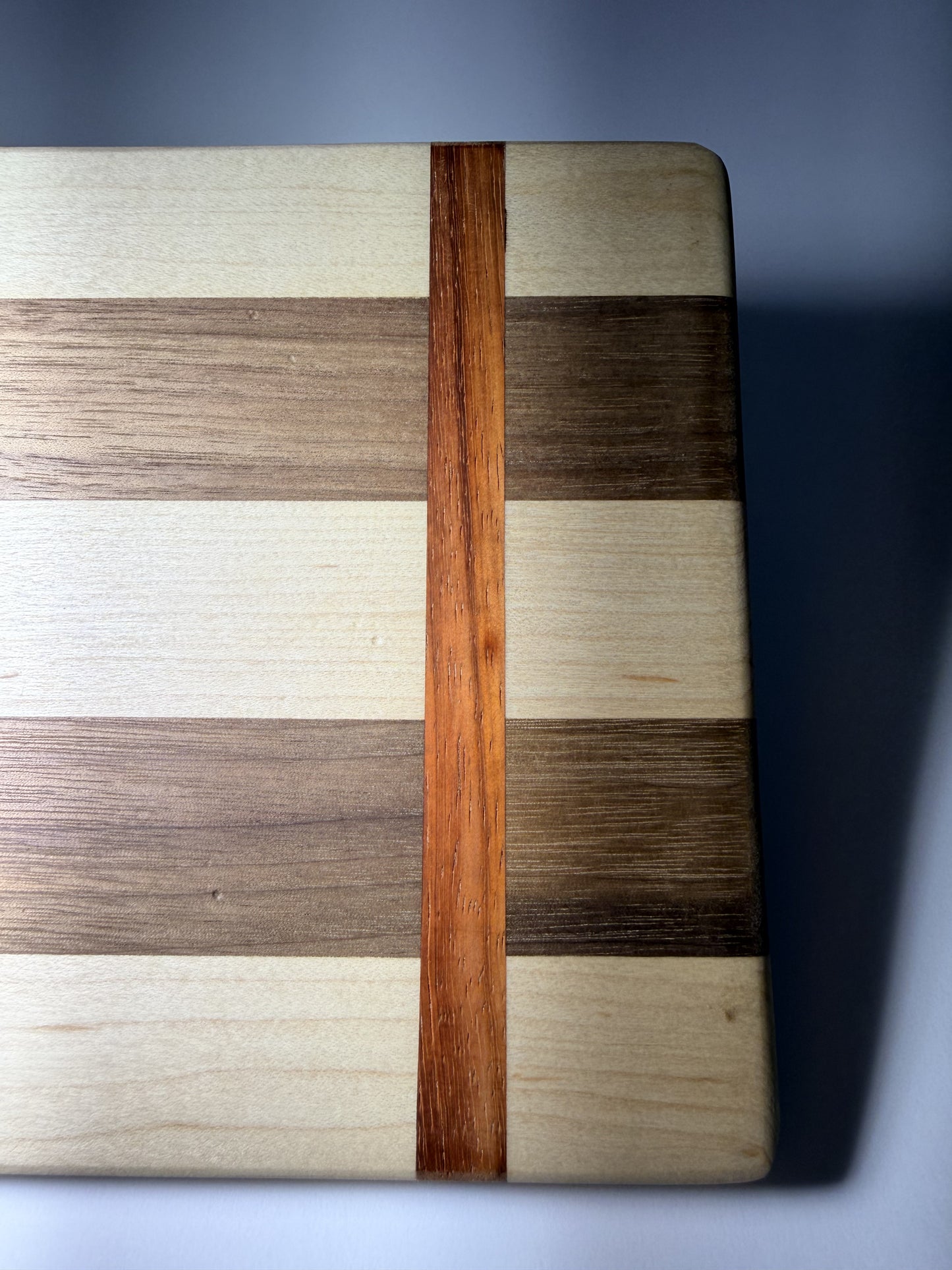 Straight padauk line crossing walnut and maple stripes — corner close-up