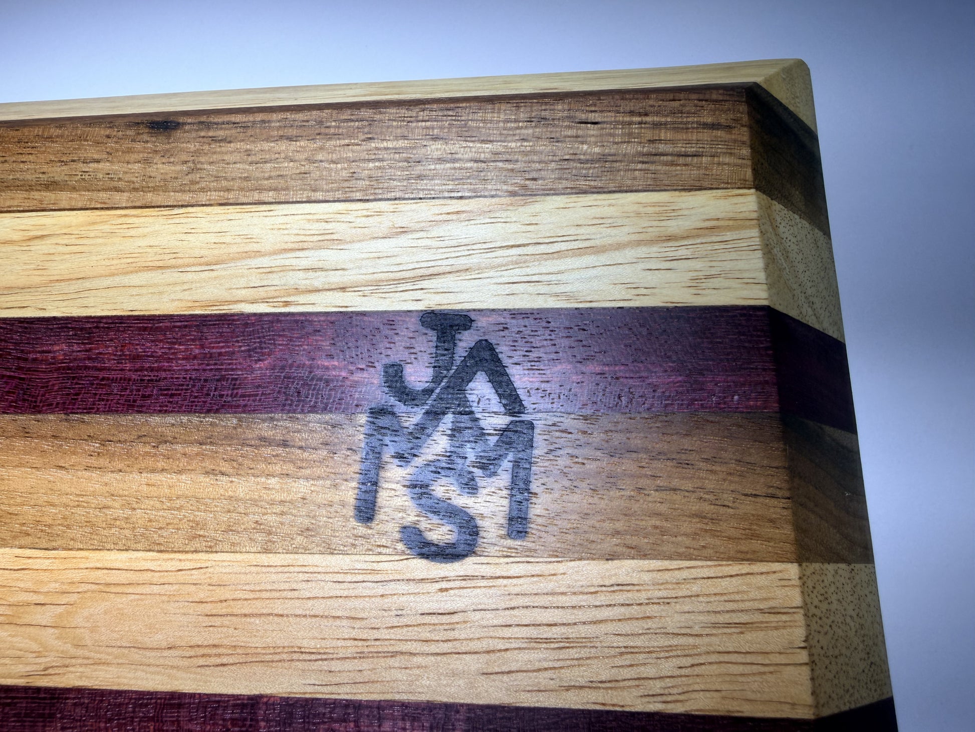 JMMS branded logo on purpleheart and oak grain — close-up