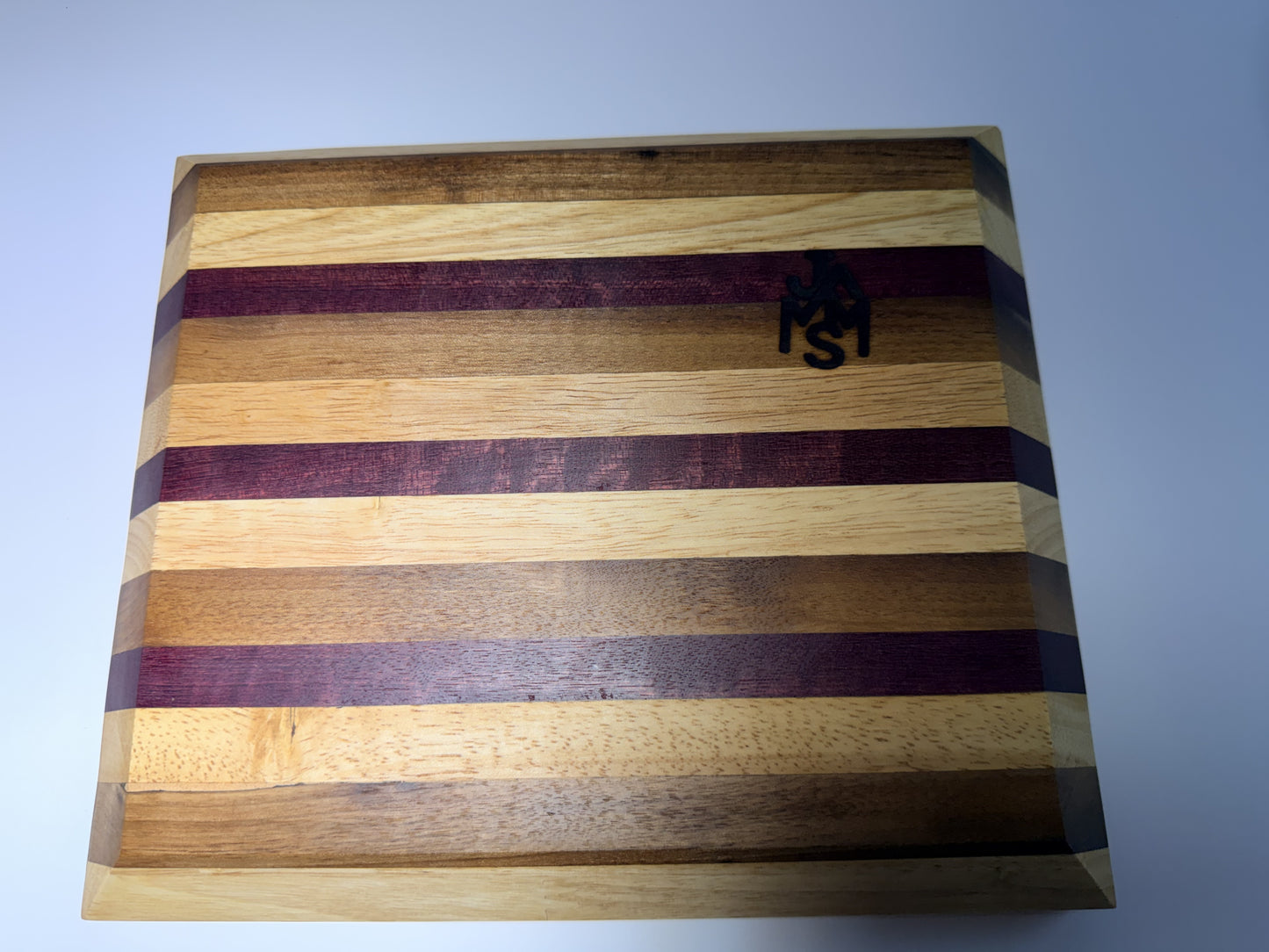 Striped cutting board with JMMS logo — angled edge view
