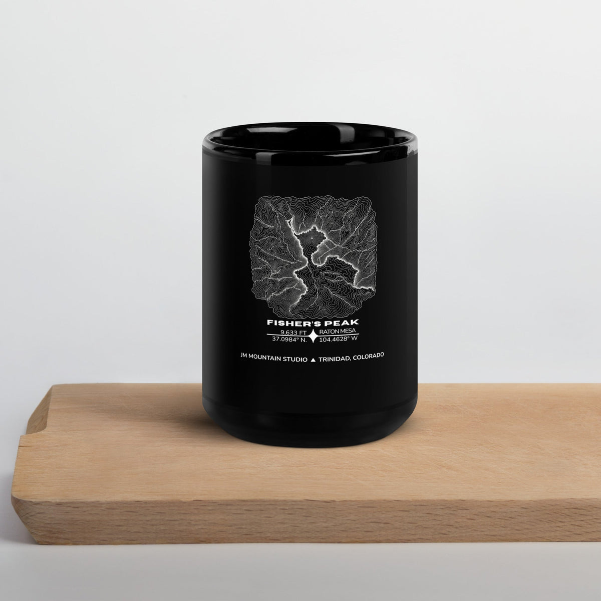 JM Mountain Studio black glossy ceramic mug featuring a white topographic map print of Fisher's Peak, Colorado.